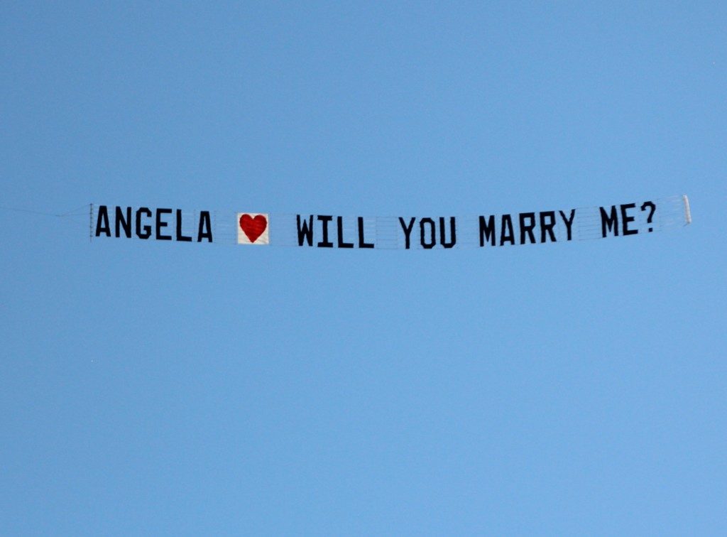 A marriage proposal written across the sky with a plane towing a banner